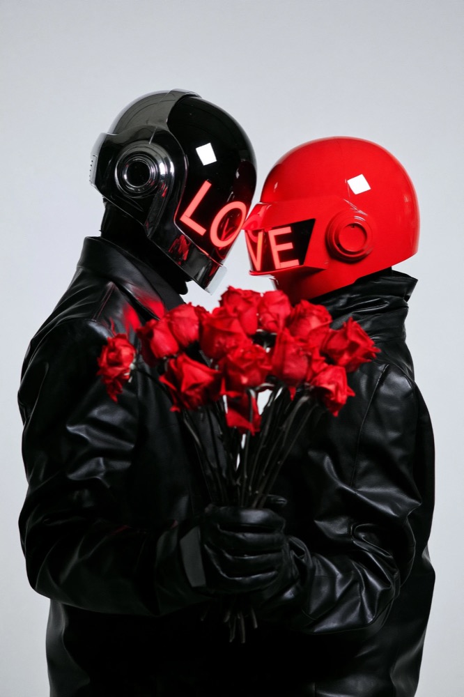 Two figures in black leather and helmets, one black and one red, lean together over red roses, LOVE lit across their visors
