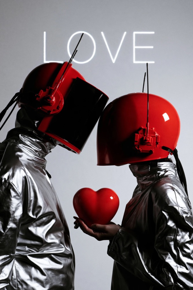 Two figures in silver coats and red helmets lean toward each other, one holding a red heart, under a LOVE sign