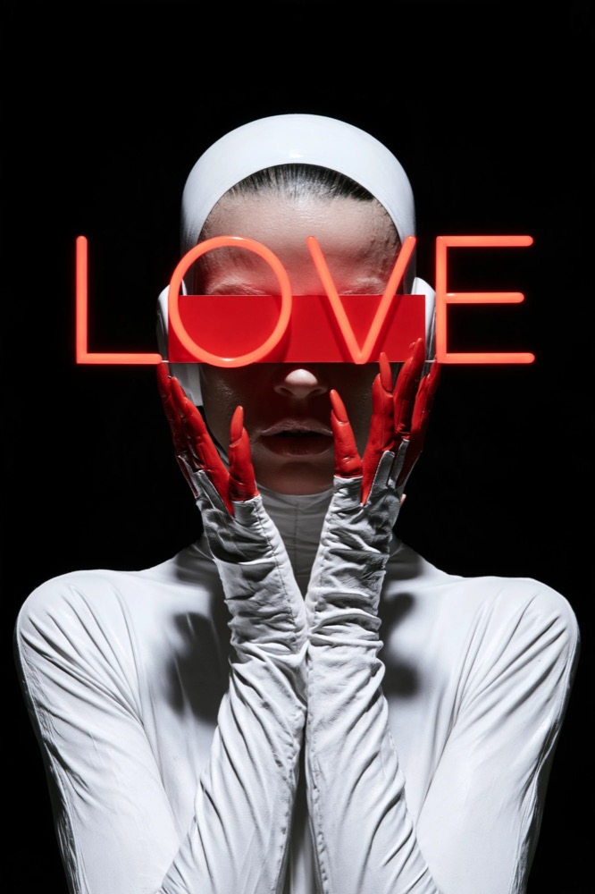 A figure in white with a red band over the eyes and red-tipped gloves, a red neon LOVE across the face