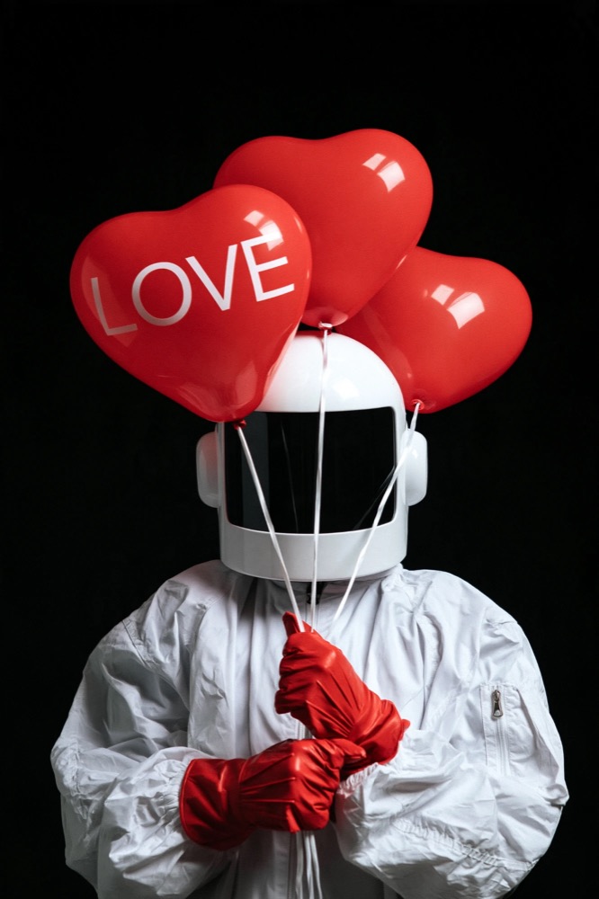 A figure in white with a white helmet and red gloves holds three red heart balloons, one reading LOVE