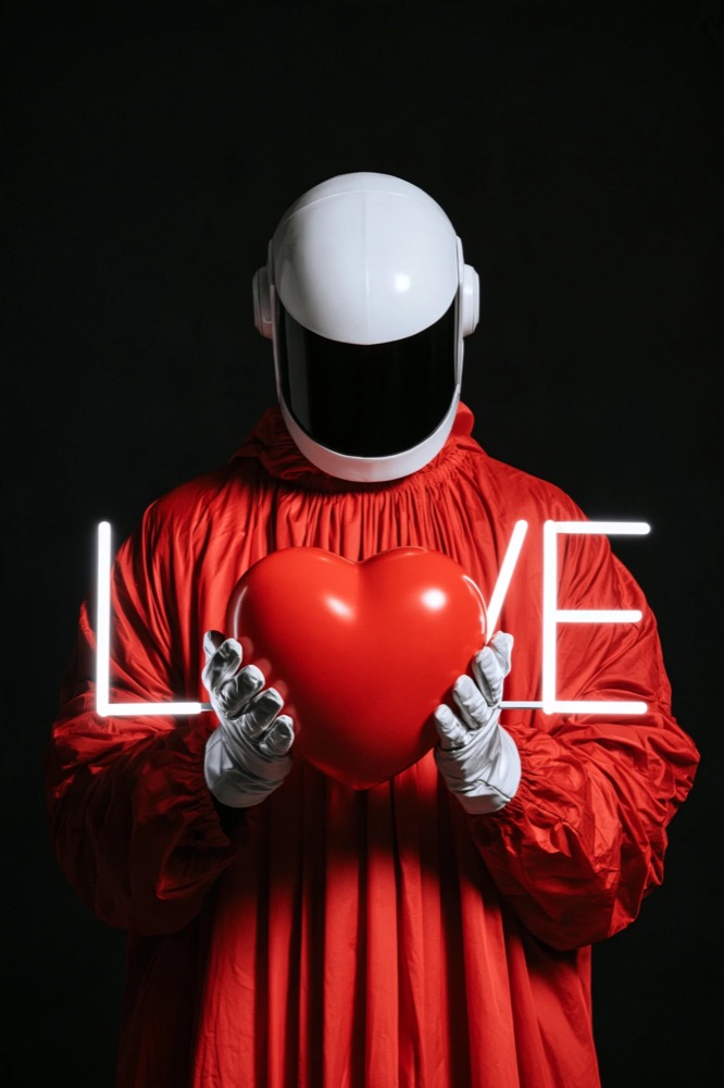 A figure in a red robe and white helmet holds a red heart that forms the O of a white neon LOVE
