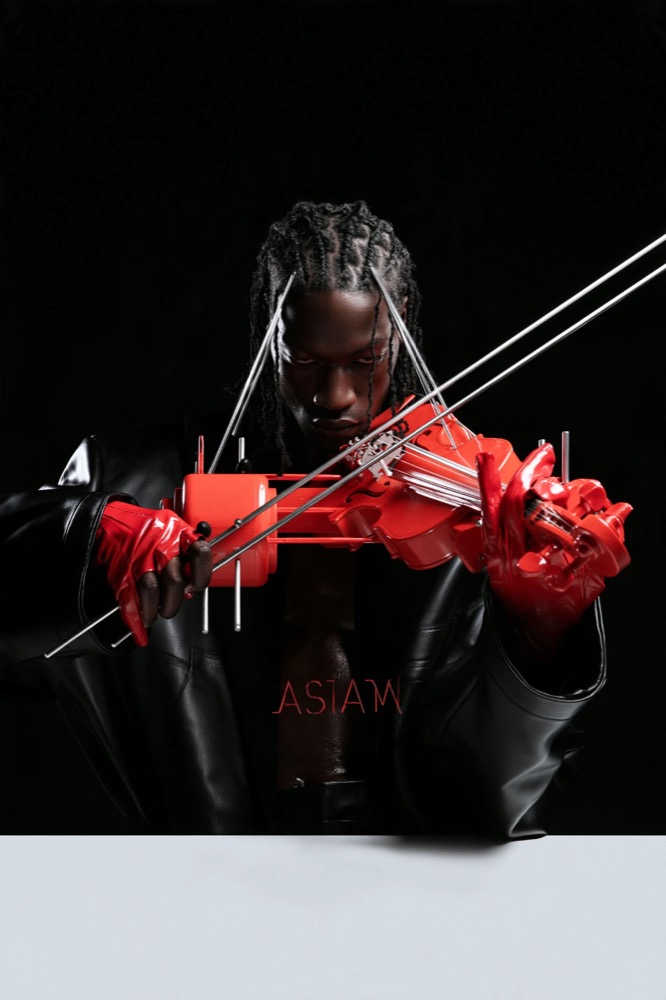 A man in black leather plays a red violin with metal rods across his face