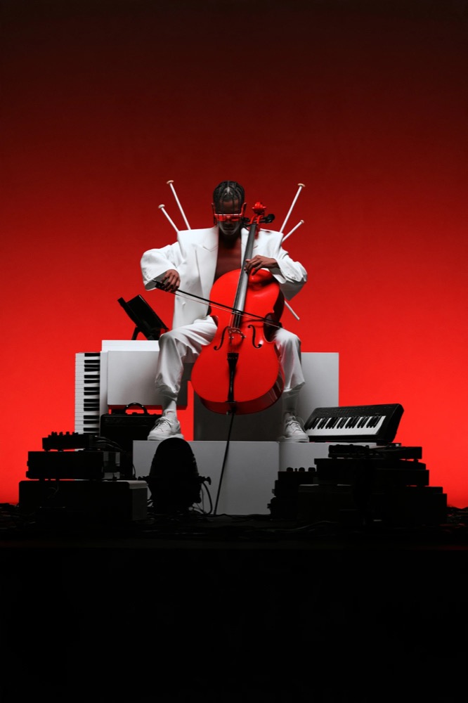 A man in a white suit and red visor plays a red cello on white blocks against a red glow