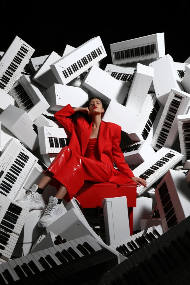 A woman in a red suit reclines with eyes closed on a pile of white keyboards