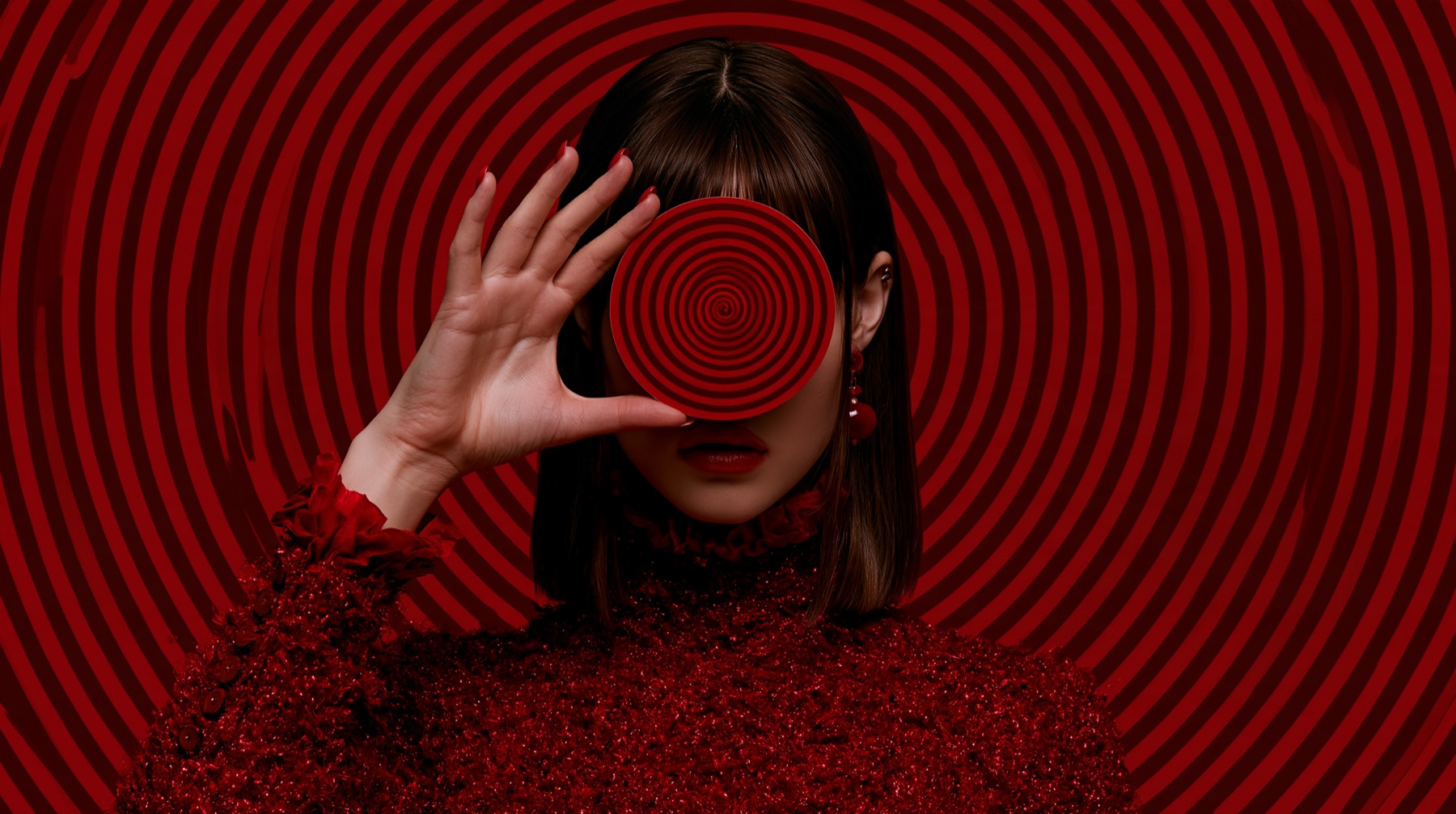 A woman holds a red spiral disc over her eye against a red spiral background